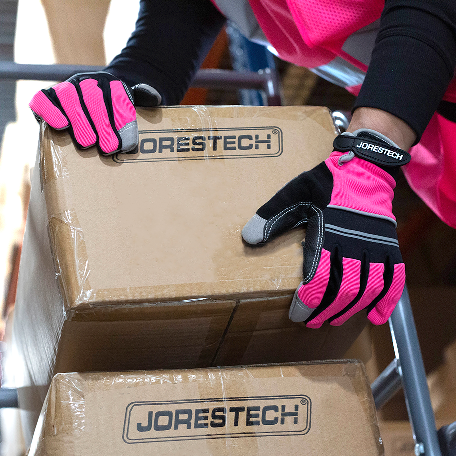 Worker wearing the pink JORESTECH safety work gloves and a pink safety vest . This person is in a ladder lifting heavy brown card boxes