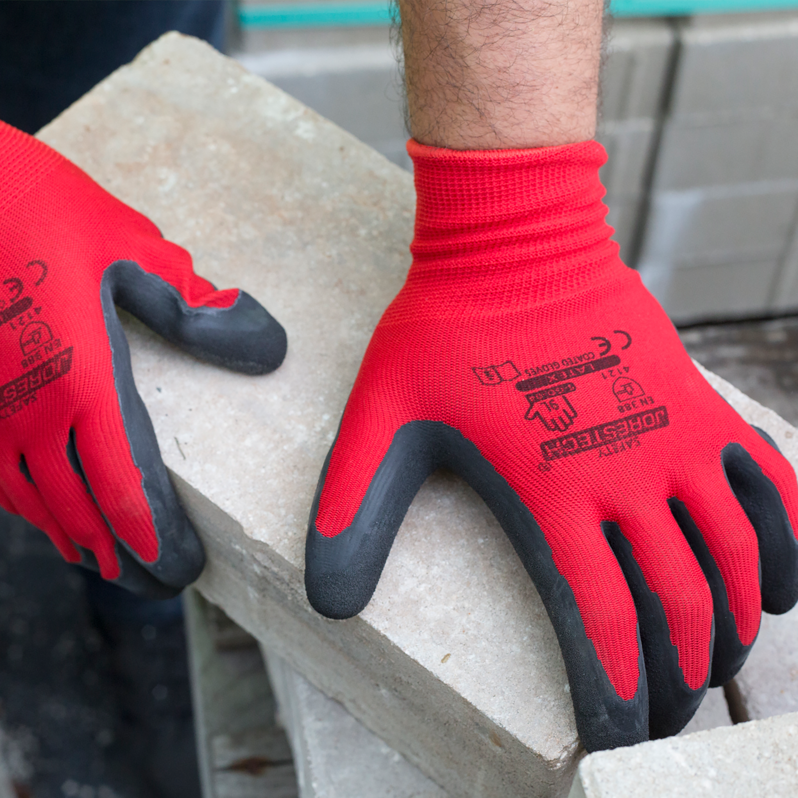Hands of worker wearing the red and black JORESTECH work gloves with latex dipped palms used for construction for carrying heavy rustic cement bricks