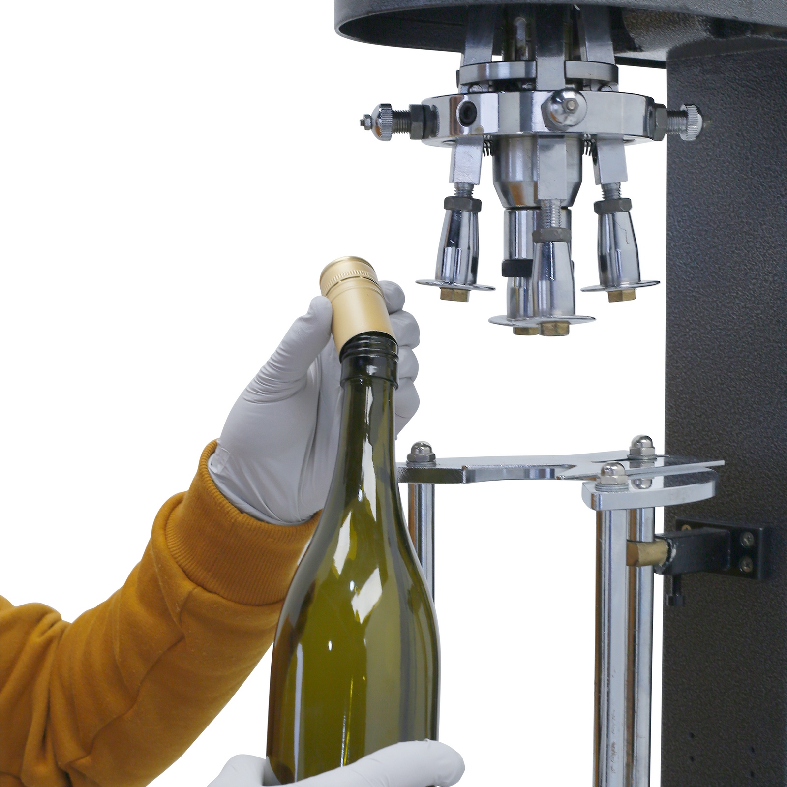 operator wearing yellow shirt and white gloves and inserting a metal cap into the bottle before closing with the grey table top JORESTECH bottle capper