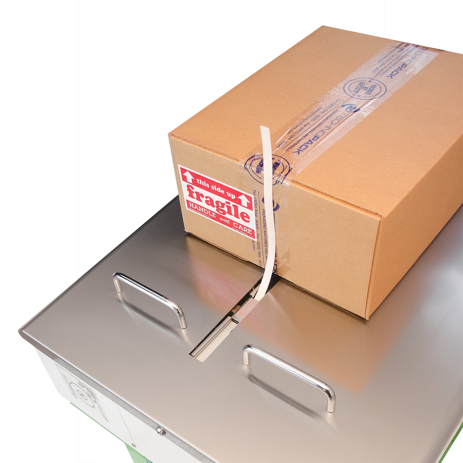 Close up of the stainless steel working are of the Strapping Machine. Strap is coming out of the supplying track and a card box is positioned to be strapped