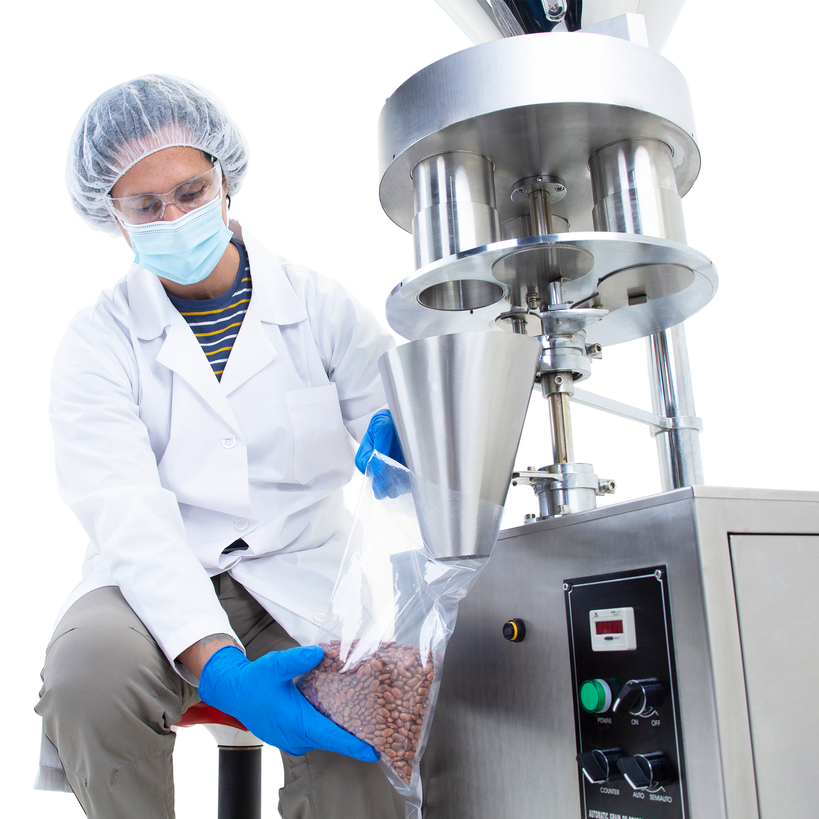 An operator wearing an assortment of personal protection equipment holding a clear plastic bag under the dispensing cone while the gravity volumetric filler releases granular product with accuracy