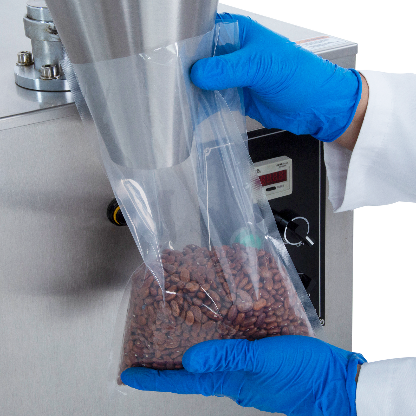 Close-up of the hands of a person holding a clear plastic bag under the dispensing cone of the semi automatic volumetric filler while it releases 1000ml of free-flowing beans with accuracy