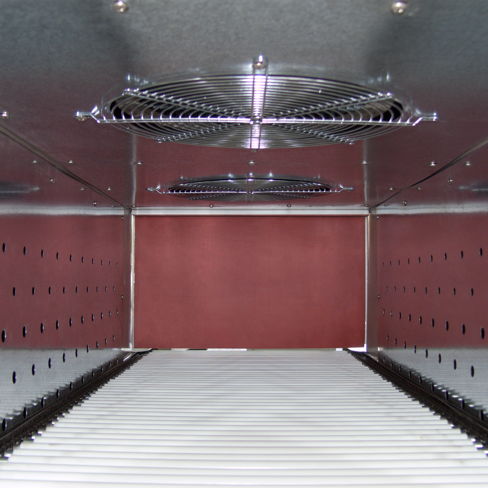 Detail of he interior of the heat shrink oven showing the heating chamber, punctured stainless steel walls, stainless steel grids for the heating fans, a roller conveyor and the exit heat tunnel curtain of  the Jorestech shrink wrapper tunnel of 20x12 inches
