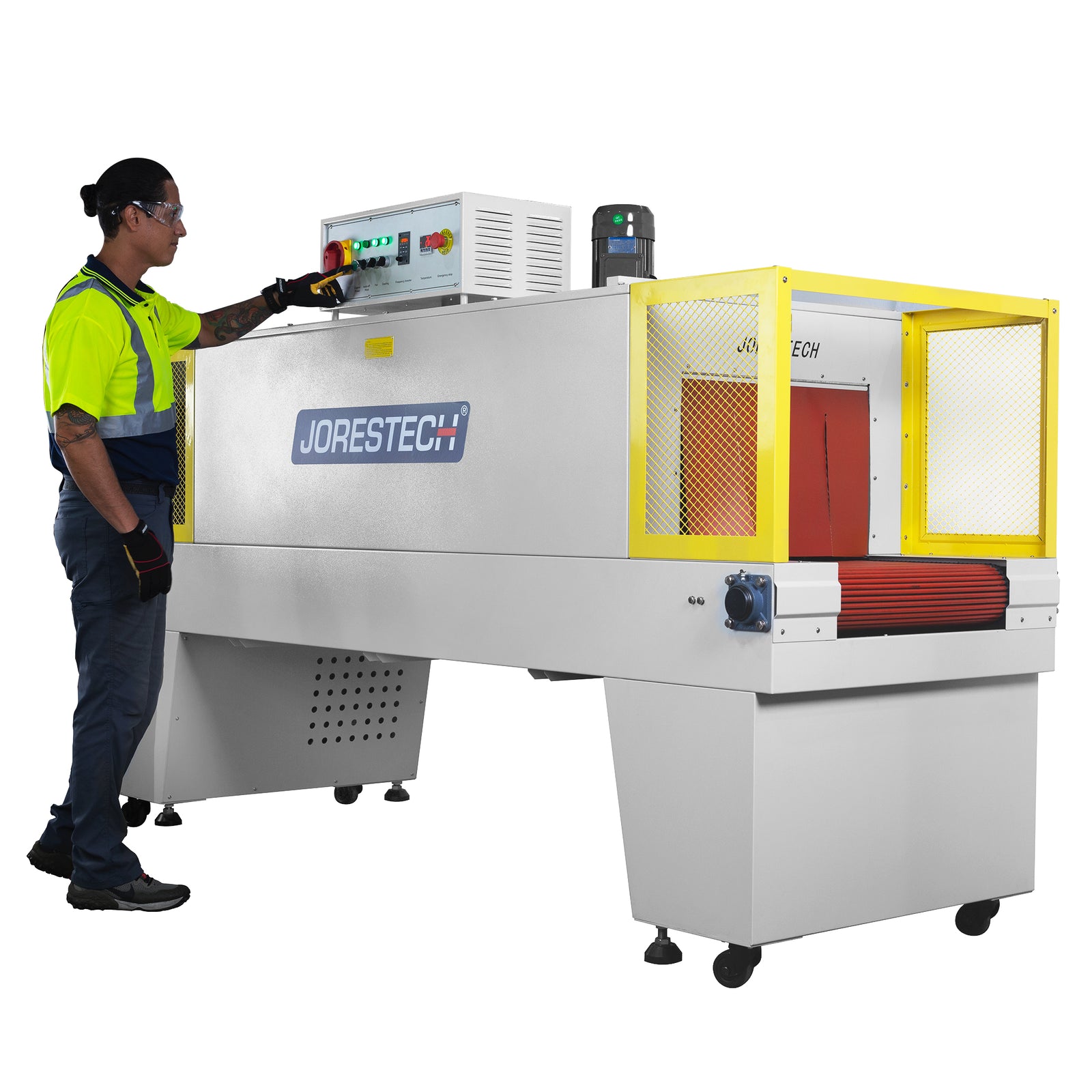 JORESTECH heat shrinking tunnel being operated by a man wearing a high visibility yellow shirt and high-impact safety glasses over a white background. He is pressing a button on the machine's control panel to stablish the conveyor's speed and temperature need in the tunnel. Three green lights on the control panel are lit up, machine is almost ready to start shrinking products.