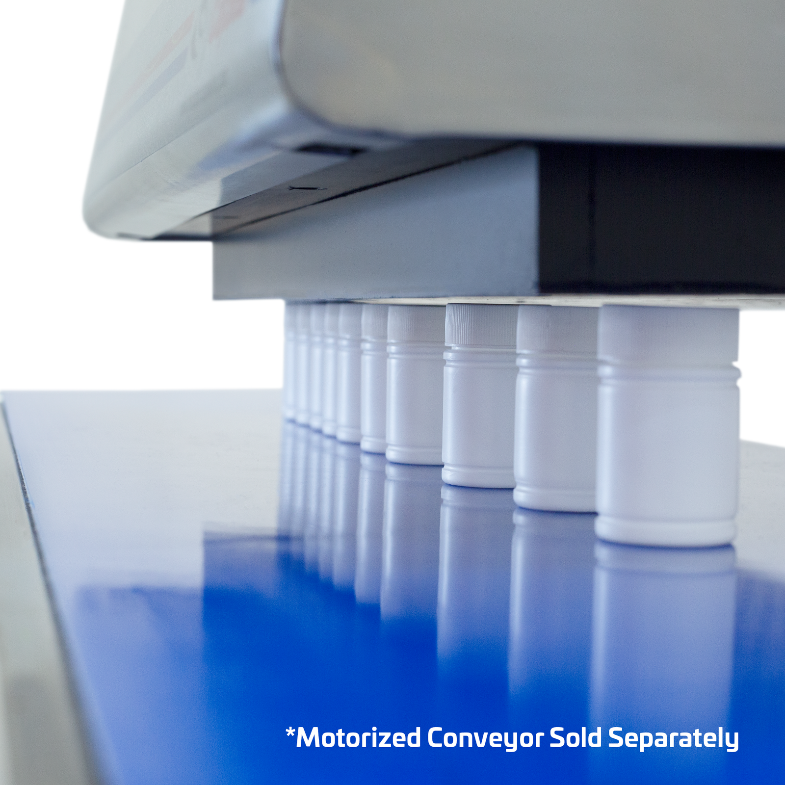 White plastic containers positioned on top of a motorized conveyor and  under the head of the Induction sealer.  The machine is producing heat to get the induction liner sealed acting as a magnetic seal. Cal out reads: Motorized conveyor sold separately