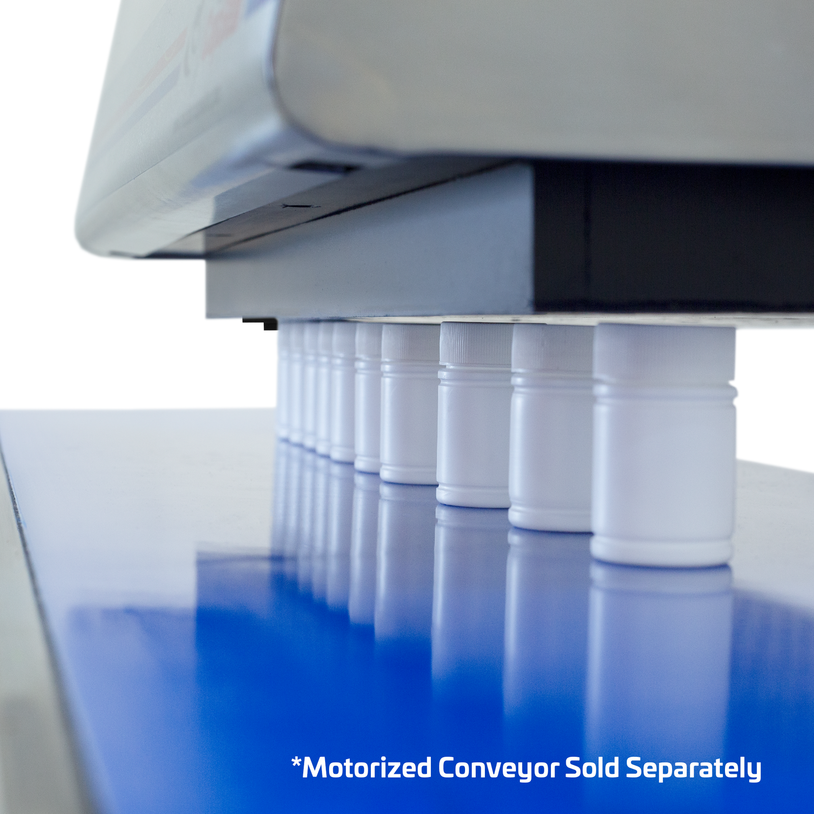 White plastic containers positioned on top of a motorized conveyor and  under the head of the Induction sealer.  The machine is producing heat to get the induction liner sealed acting as a magnetic seal. Cal out reads: Motorized conveyor sold separately