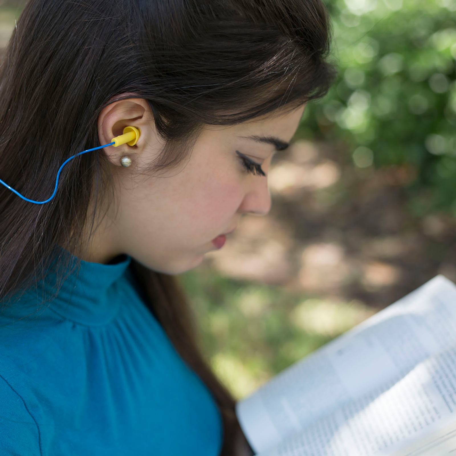 A student wearing corded yellow and blue earplugs while reading 