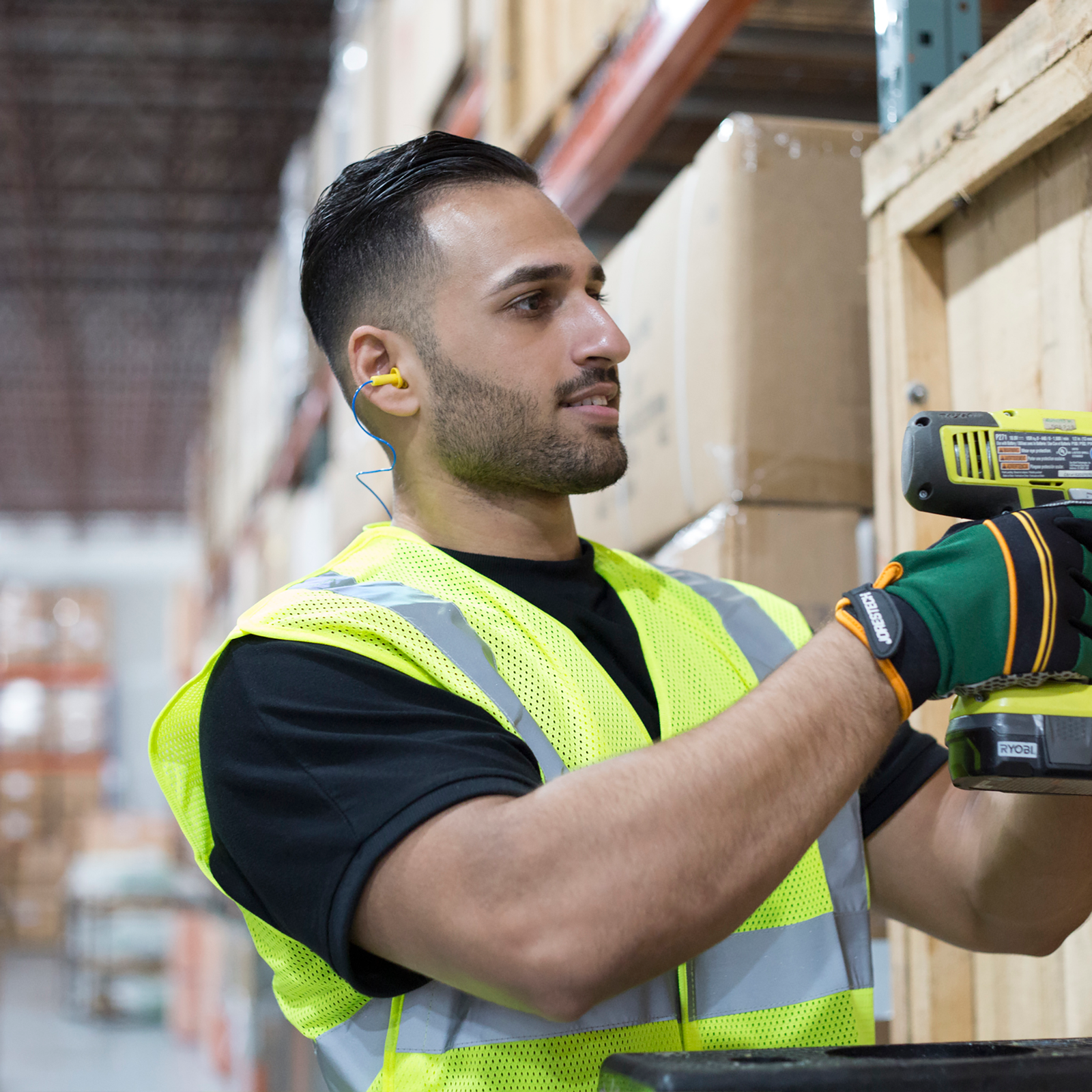 Man working wearing silicon corded earplugs for noise reduction while operating a loud power tool in a warehouse