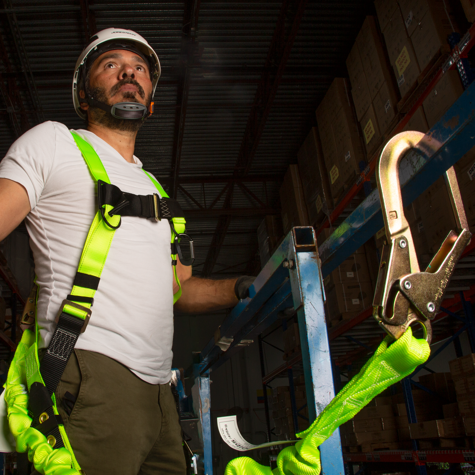 Man wearing a harness with the lime JORESTECH single leg internal shock absorbing lanyard with snap hook and scaffolding attached to his safety harness. 