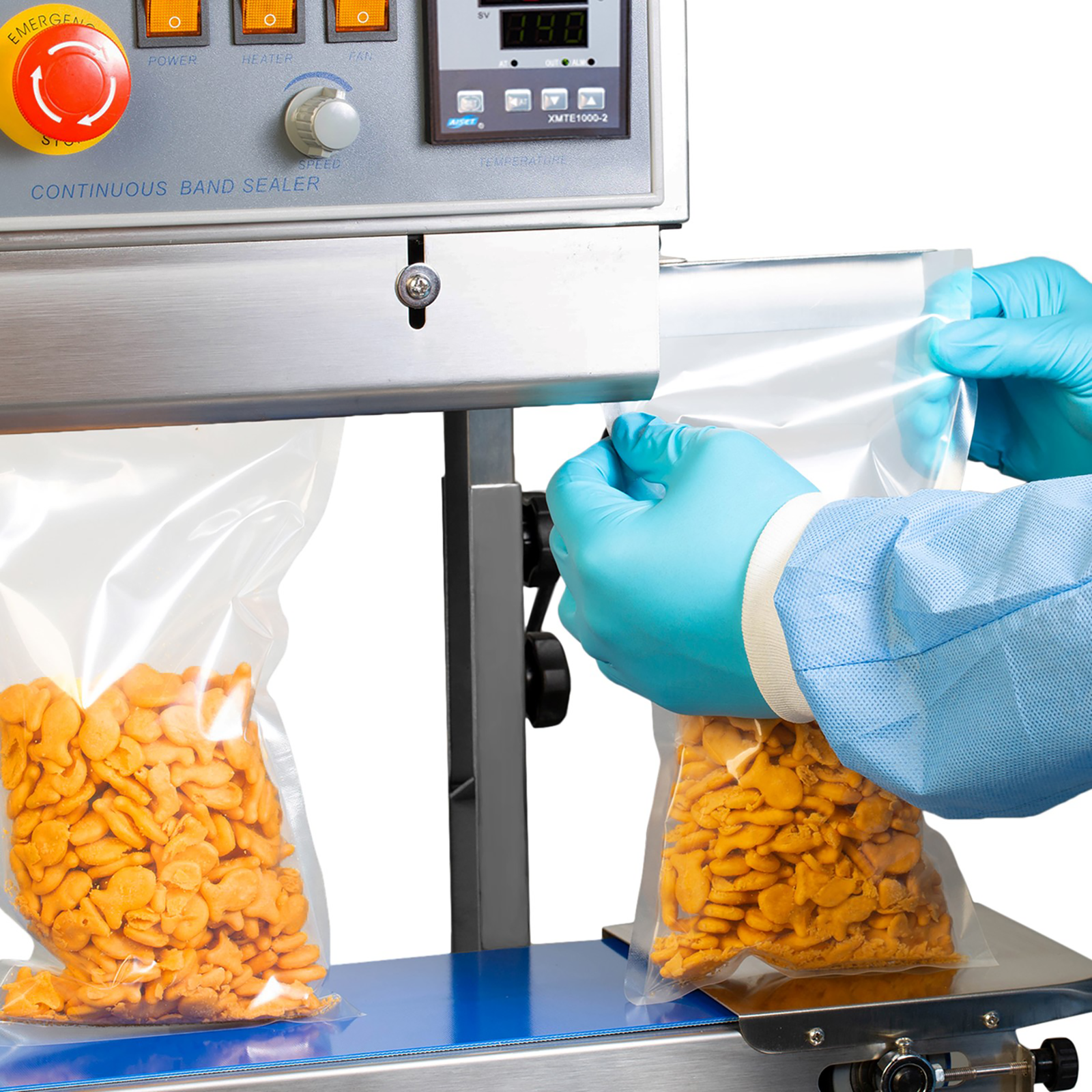operator wearing blue gloves inserting several plastic bags with orange crackers in a vertical JORESTECH stainless-steel continuous band sealing machine