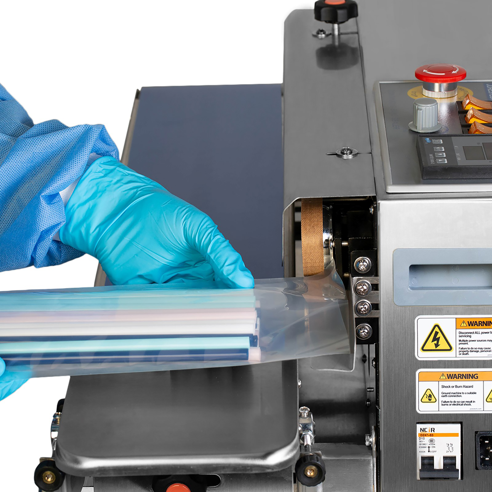an operator wearing disposable blue gloves inserting a clear bag filled with multi-colored straw in JORESTECH continuous band sealer set horizontally to seal the bag closed