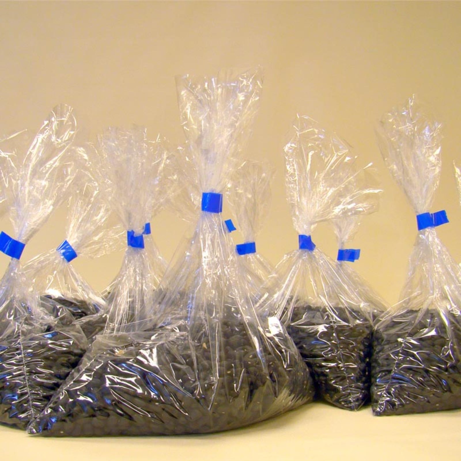 Several plastic bags filled with black dry beans closed with blue self adhesive tape after using the stainless steel manual bag neck taper