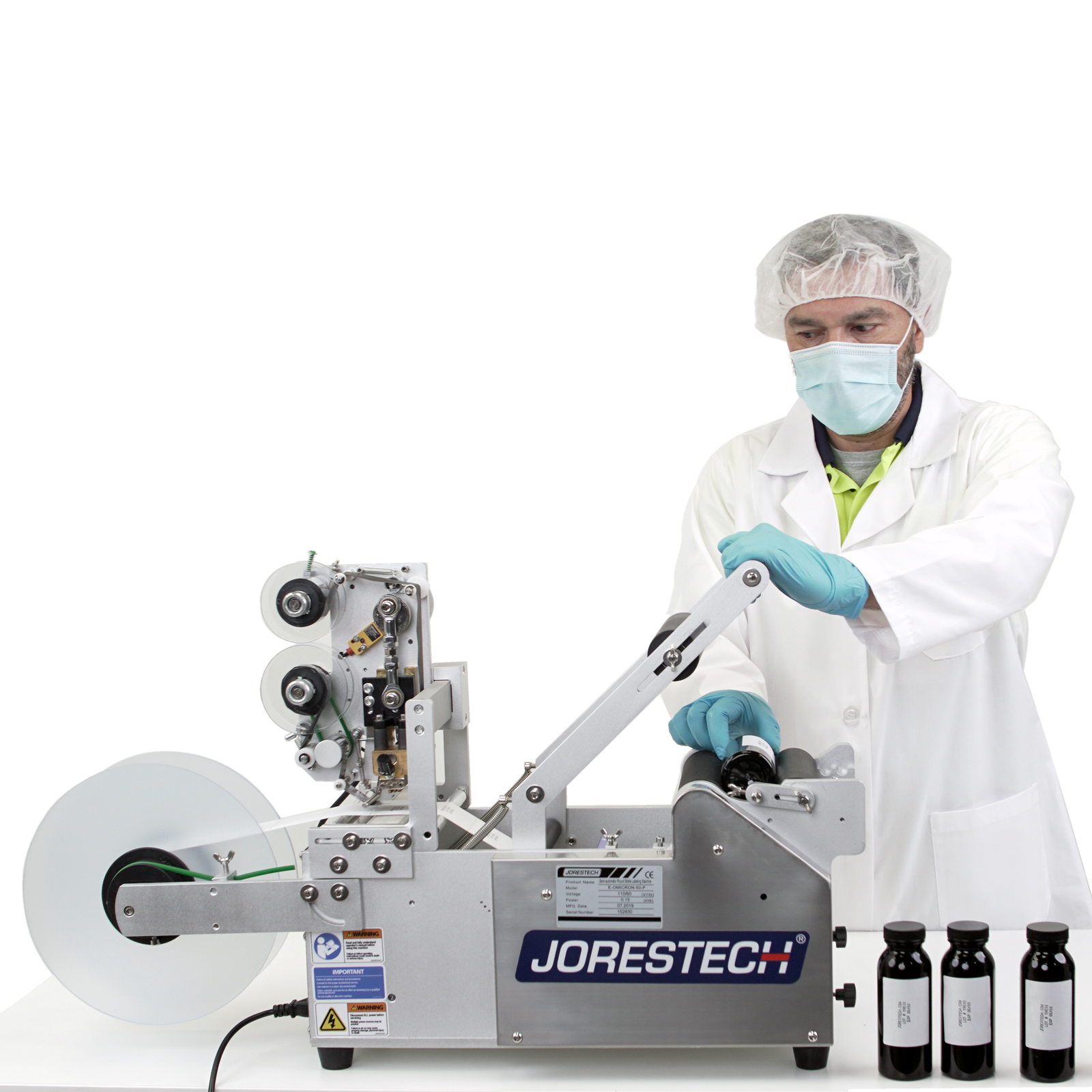 A man wearing personal protection equipment. He is operating the Jorestech semi automatic labeling machine by applying labels to round containers. A set of 3 bottles is shown with printed labels with written information
