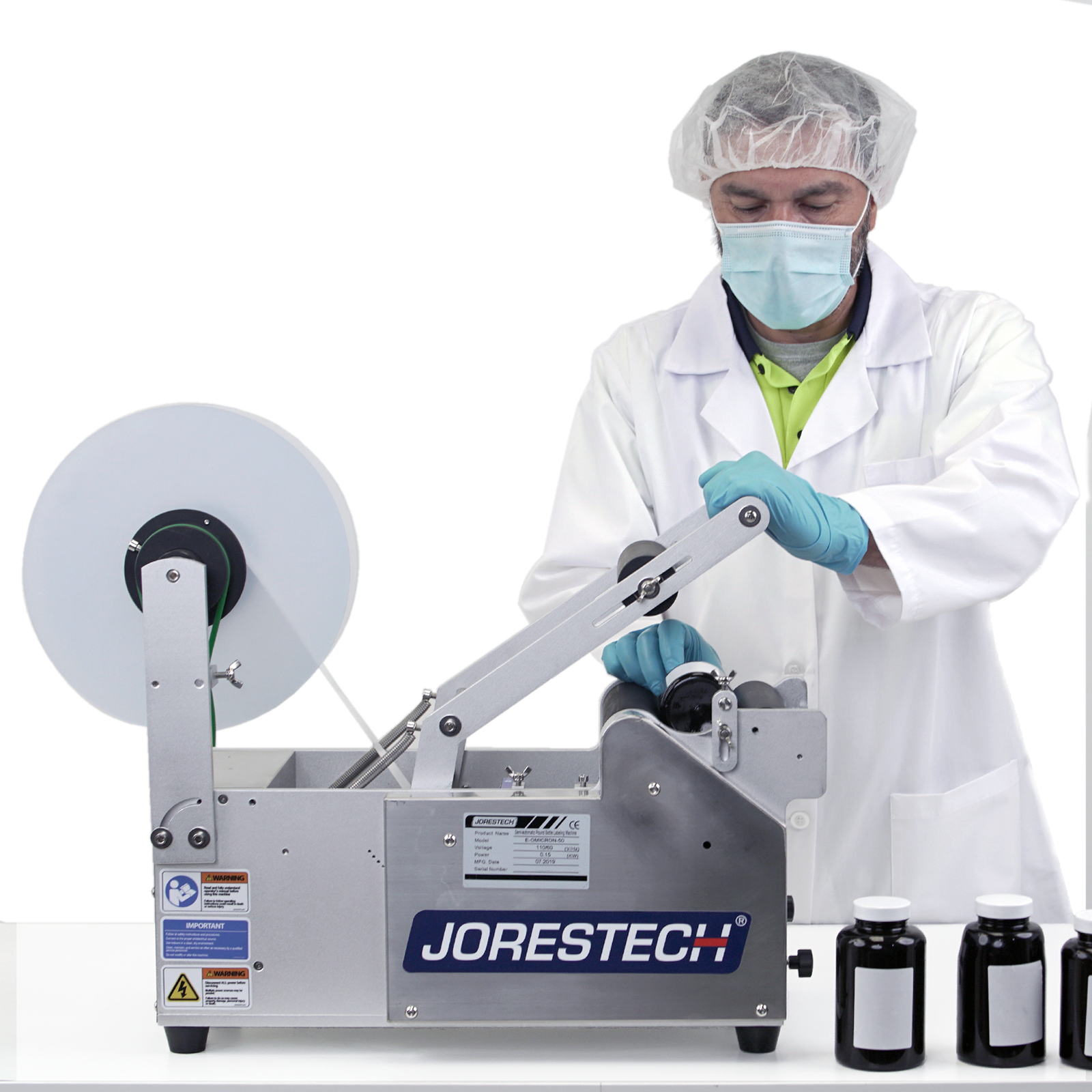 Man wearing personal protection equipment while operating the JORES TECHNOLOGIES® semi automatic labeling machine by pushing the activation handle to apply labels to round containers