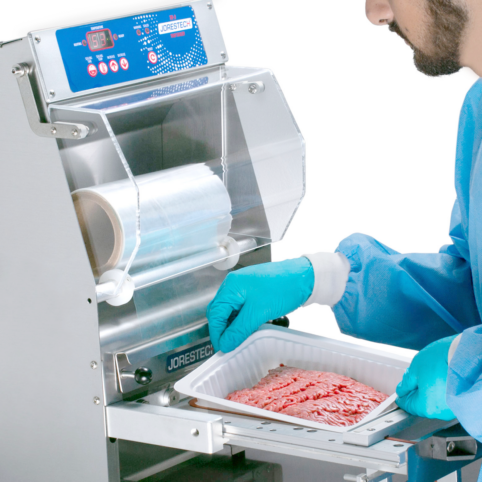operator wearing disposable clothing inserting a white plastic tray filled with raw meat into stainless steel packaging tray sealer