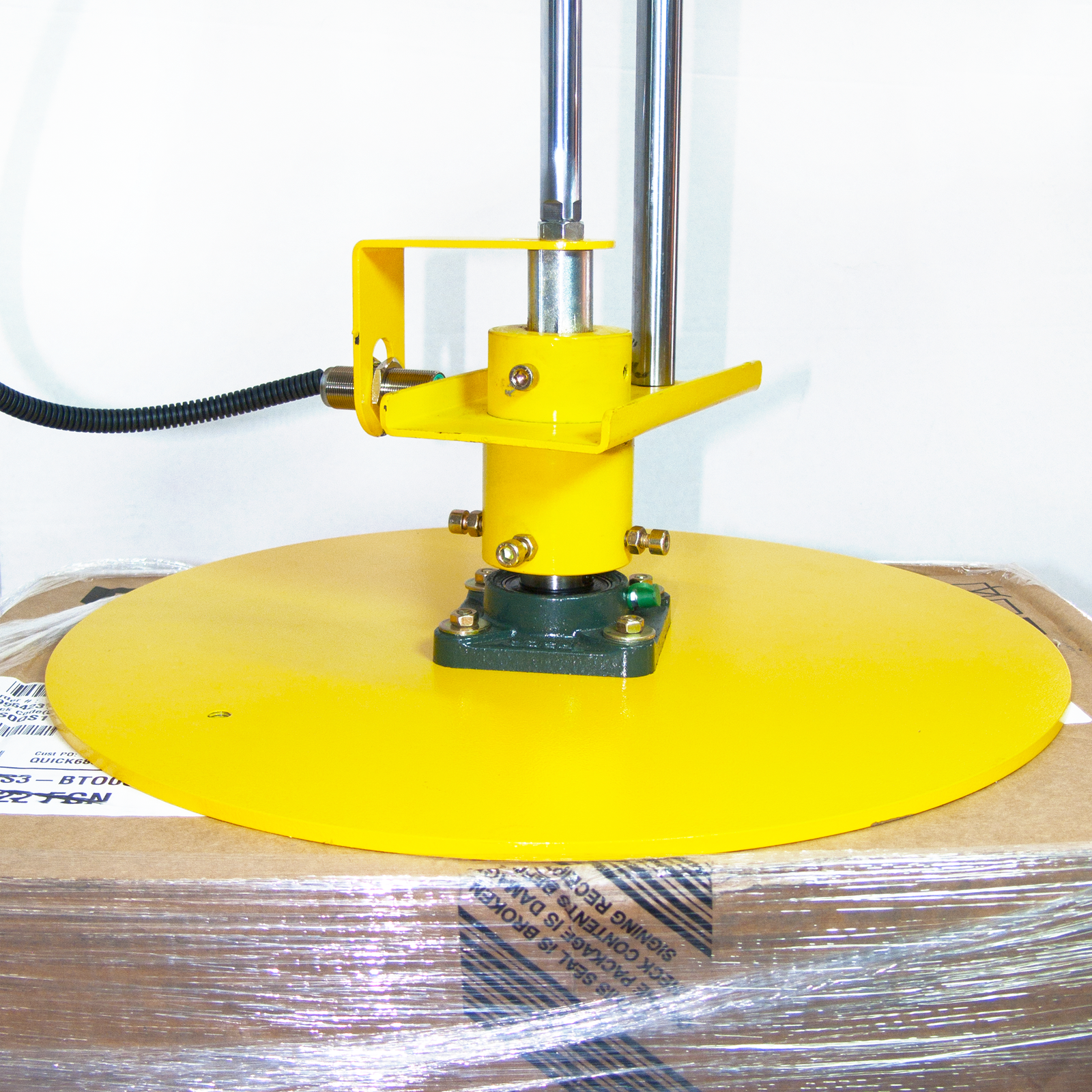 Close-up of the top pressure plate of a box stretch wrapper. It is holding down a cardboard box that is being wrapped with stretch film.