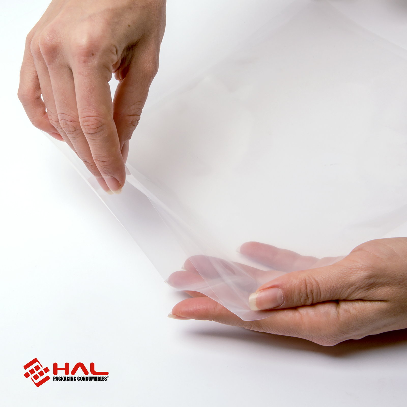 Hands of a woman opening a clear bag to show the material of the HAL vacuum sealer bags over white background