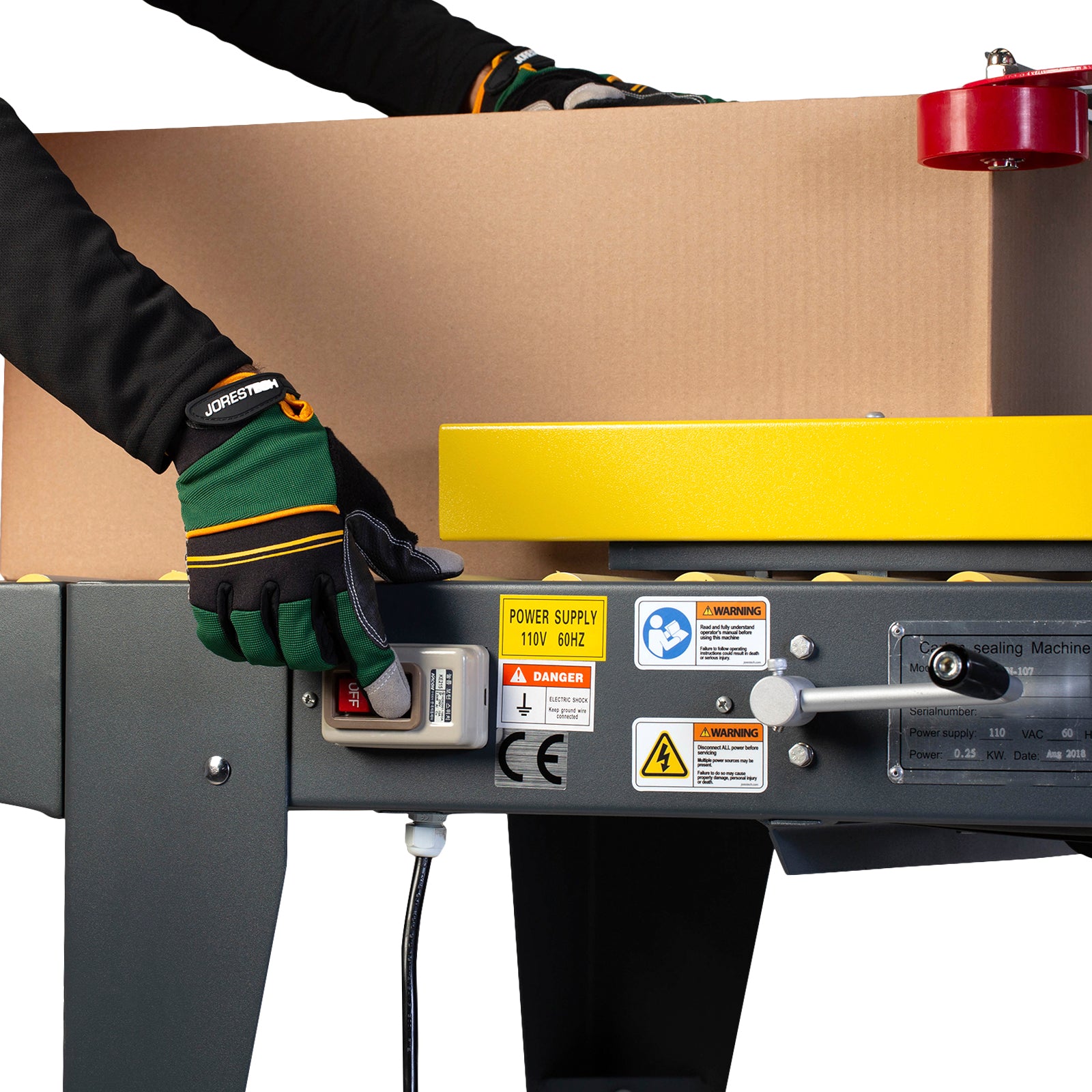 operator wearing green and orange pushing button and inserting brown cardboard box into case sealer machine with side traction
